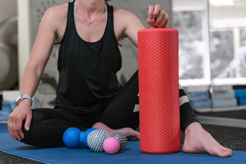 Young Sportswoman in the Gym Sits on Yoga Mat with Different Types of Myofascial Rolls. Equipment for MFR. Roller for Physiotherapy.